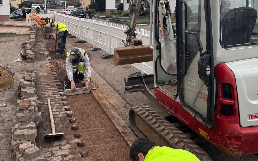 Operarios reponiendo el pavimento junto a la zanja con miniexcavadora en obra urbana